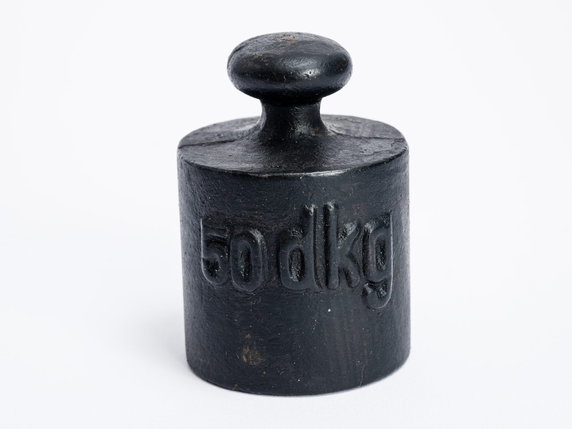 suly 50 dkg.jpg Öntöttvas, sárgaréz közepű súly. Hengeres formájú, felül gomba alakú, önmagából kialakított fogóval. Oldalán domború felirat: 50 dkg. Alján a kilátszó rézbe gyári jel van ütve.